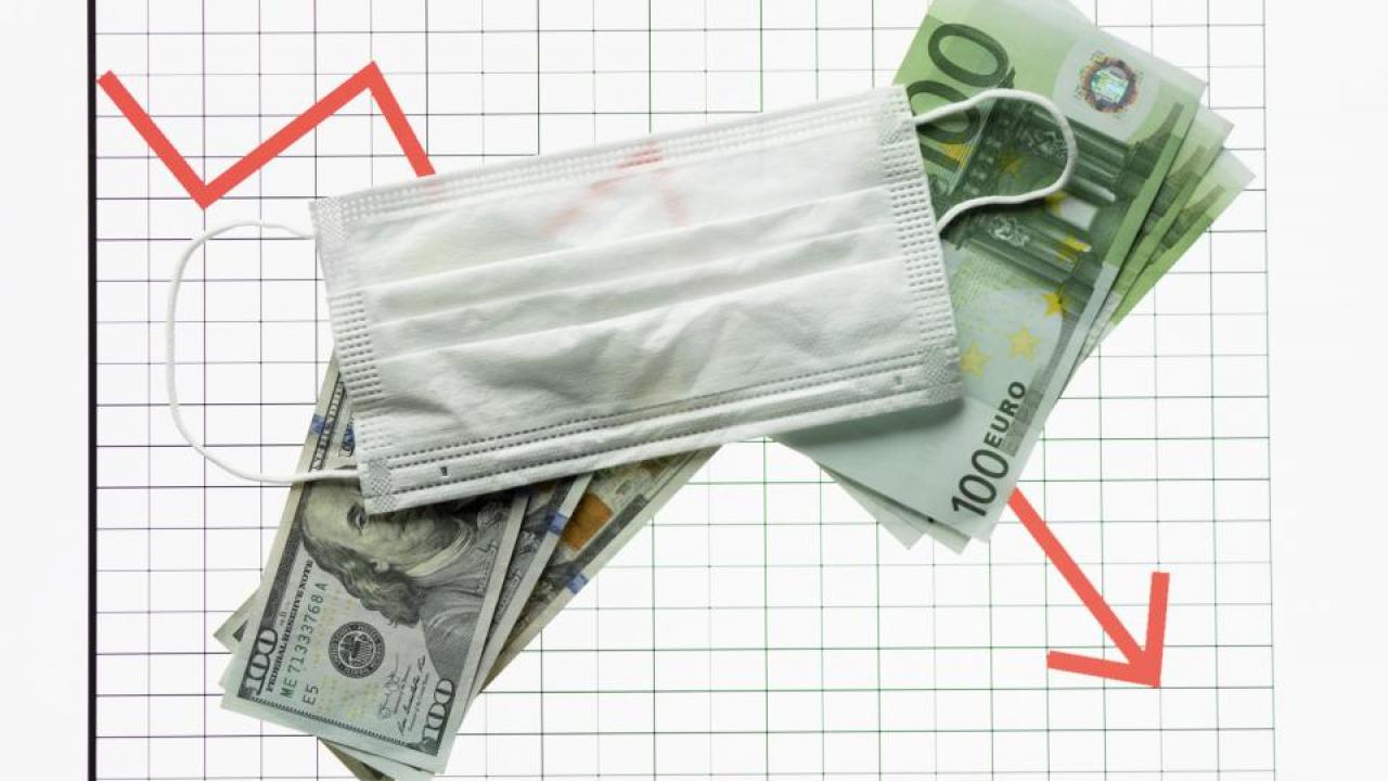 Graph showing a downward red arrow with a surgical mask on top of U.S. and European currency.