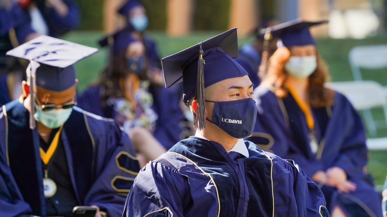 man in graduation attire and uc davis face mask